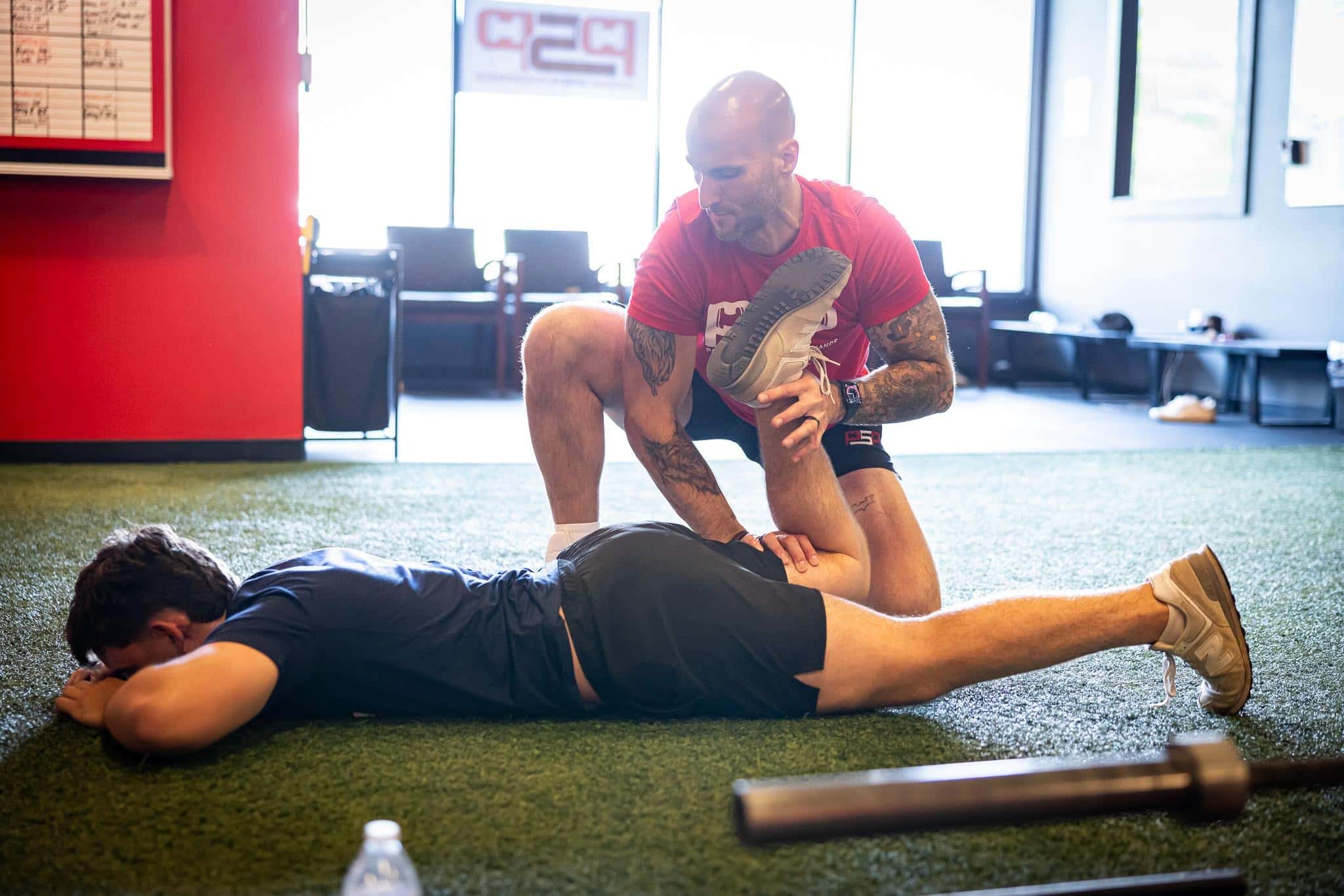 Coach assists an athlete with a hamstring stretch on indoor turf at Parsons Sports Performance.